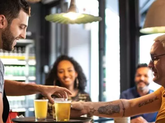 Pessoas alegres em um bar, com copos cheios de cerveja em suas mãos