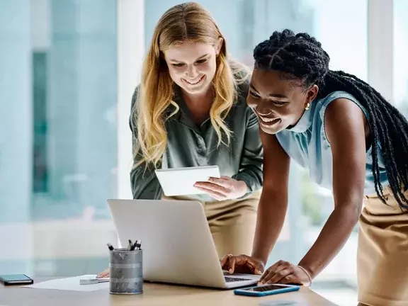 Duas empresárias diversas trabalhando juntas em um tablet digital e laptop em um escritório
