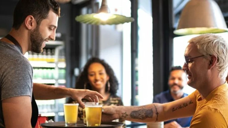 Pessoas alegres em um bar, com copos cheios de cerveja em suas mãos