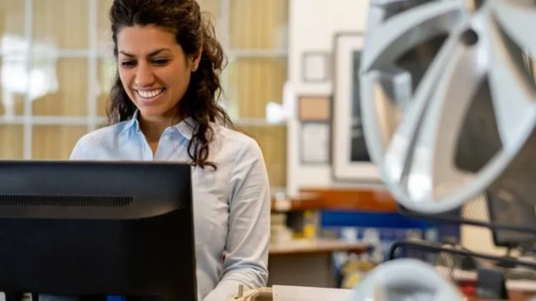 Em uma empresa automotiva, funcionária trabalha sorrindo em frente a um computador