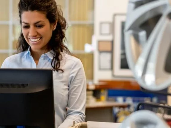 Em uma empresa automotiva, funcionária trabalha sorrindo em frente a um computador