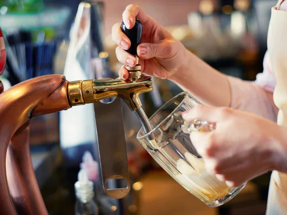 Mãos retirando chopp e colocando em copo de vidro 