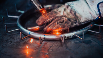 Soldagem em peça metálica com faíscas e luva de proteção.