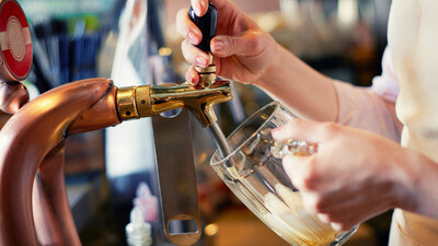 Mãos retirando chopp e colocando em copo de vidro 