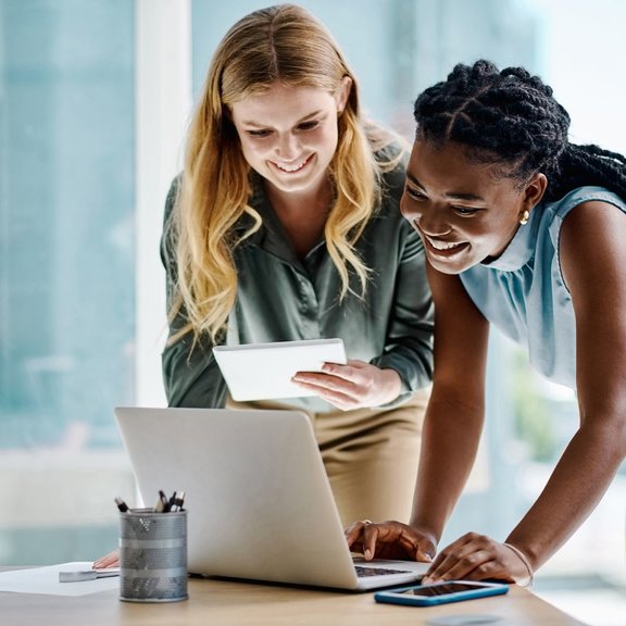 Duas empresárias diversas trabalhando juntas em um tablet digital e laptop em um escritório